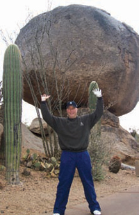 Man in desert, gesture holding up a large boulder.